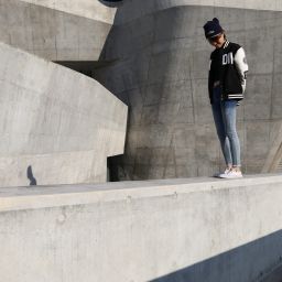 Young woman in varsity jacket on concrete wall, daring to dream.