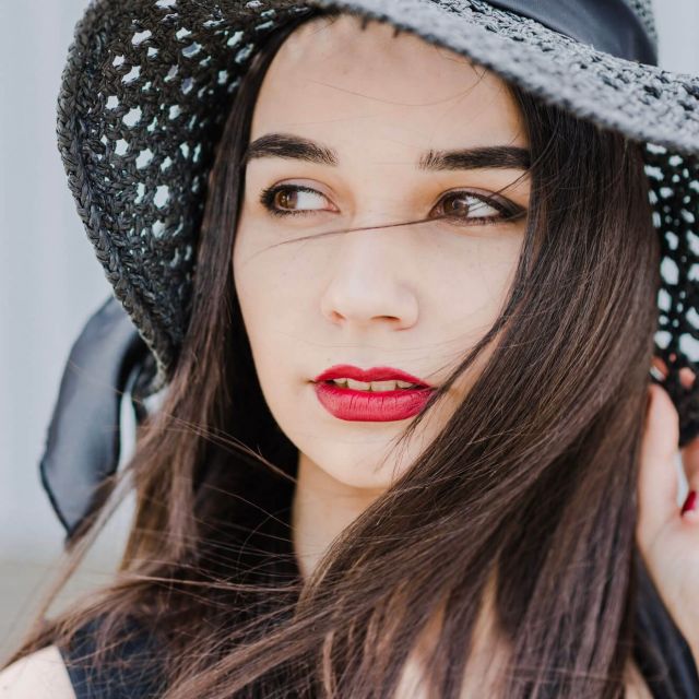 Close-up portrait of a young woman wearing a wide-brimmed hat, dreaming.