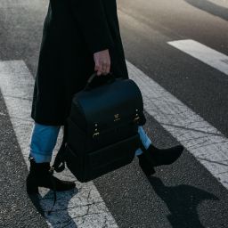 Woman crossing street, carrying black Vinta backpack. Stylish urban commute.