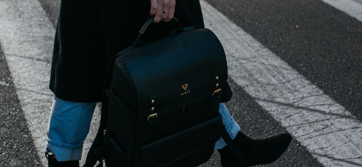 Woman crossing street, carrying black Vinta backpack. Stylish urban commute.