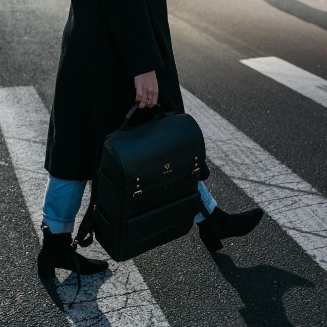 Woman crossing street, carrying black Vinta backpack. Stylish urban commute.