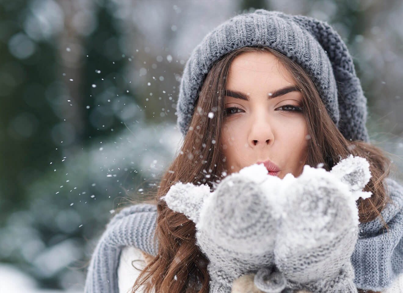 Woman blowing snow, winter fashion, grey hat and gloves