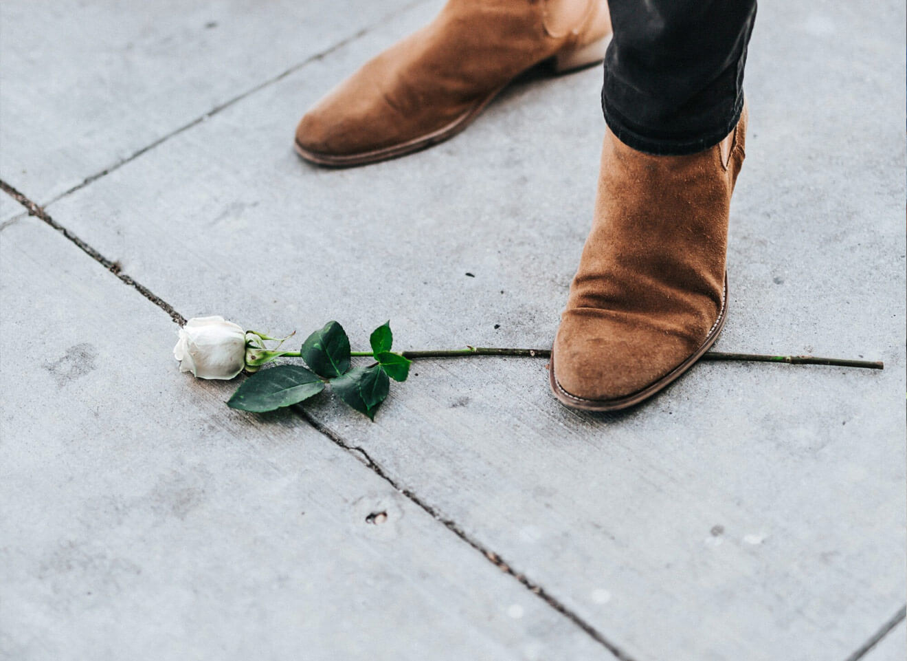 Brown suede boots and single white rose on pavement