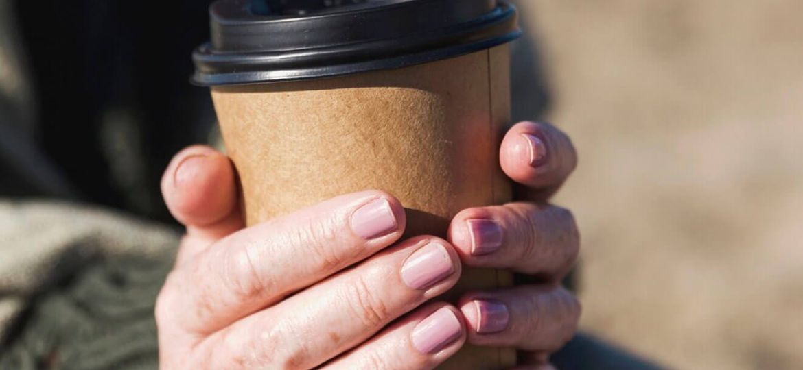 Close-up of hands holding a takeaway coffee cup.