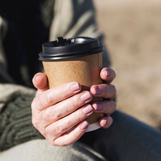 Close-up of hands holding a takeaway coffee cup.