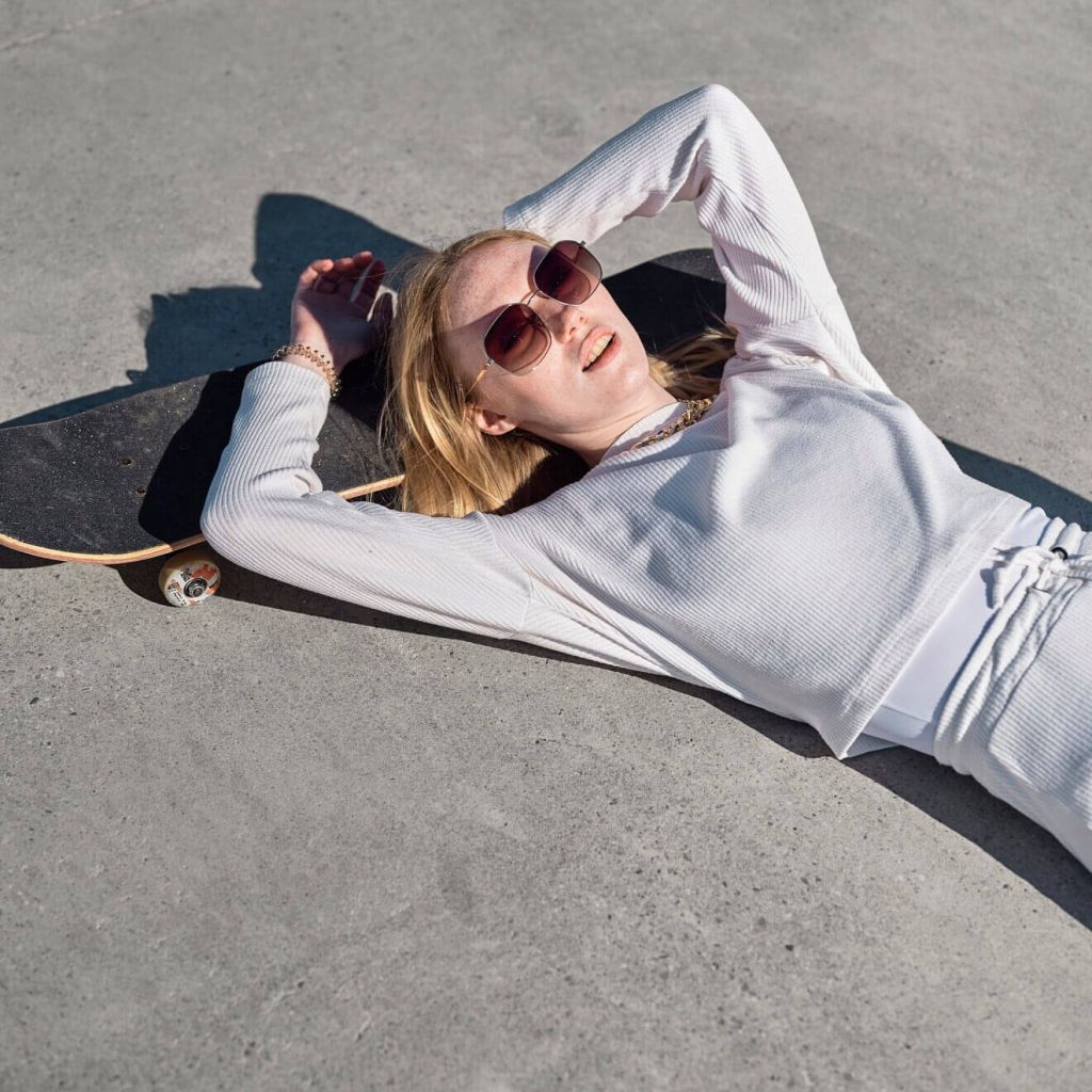Young woman in white resting on skateboard, sunglasses on, dreaming