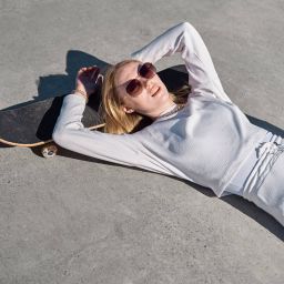 Young woman in white resting on skateboard, sunglasses on, dreaming