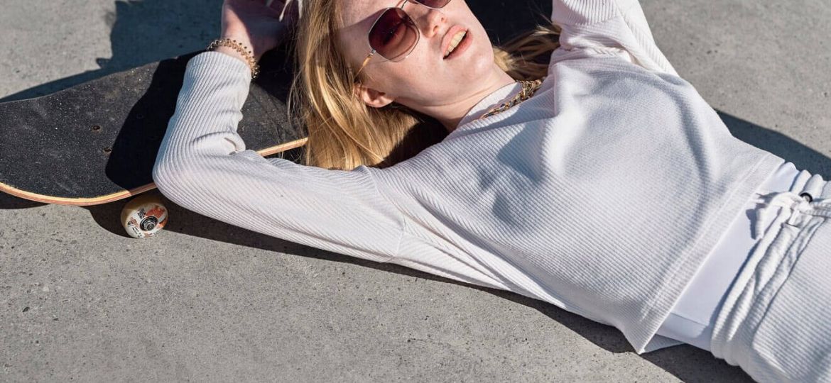 Young woman in white resting on skateboard, sunglasses on, dreaming