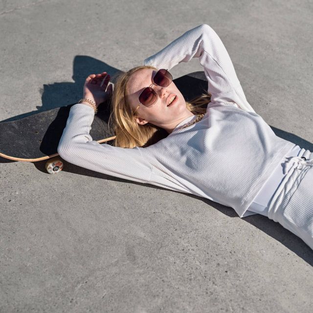Young woman in white resting on skateboard, sunglasses on, dreaming
