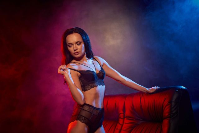 Woman in black lingerie poses on a red couch.
