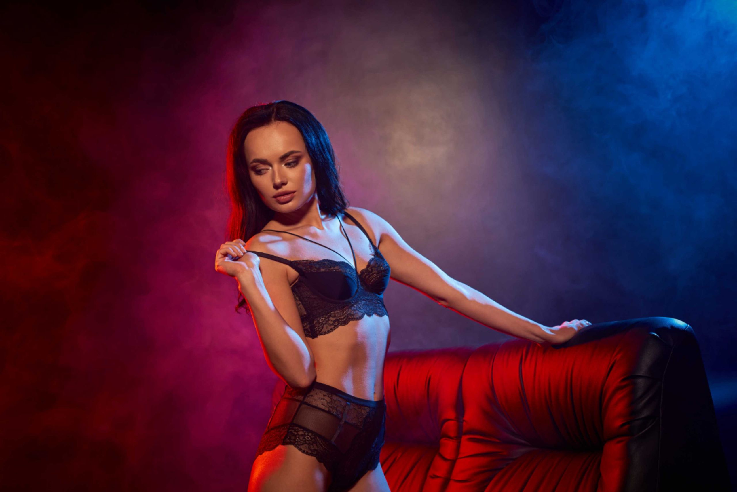 Woman in black lingerie poses on a red couch.