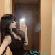 Young woman in black dress taking a selfie in a bathroom mirror.