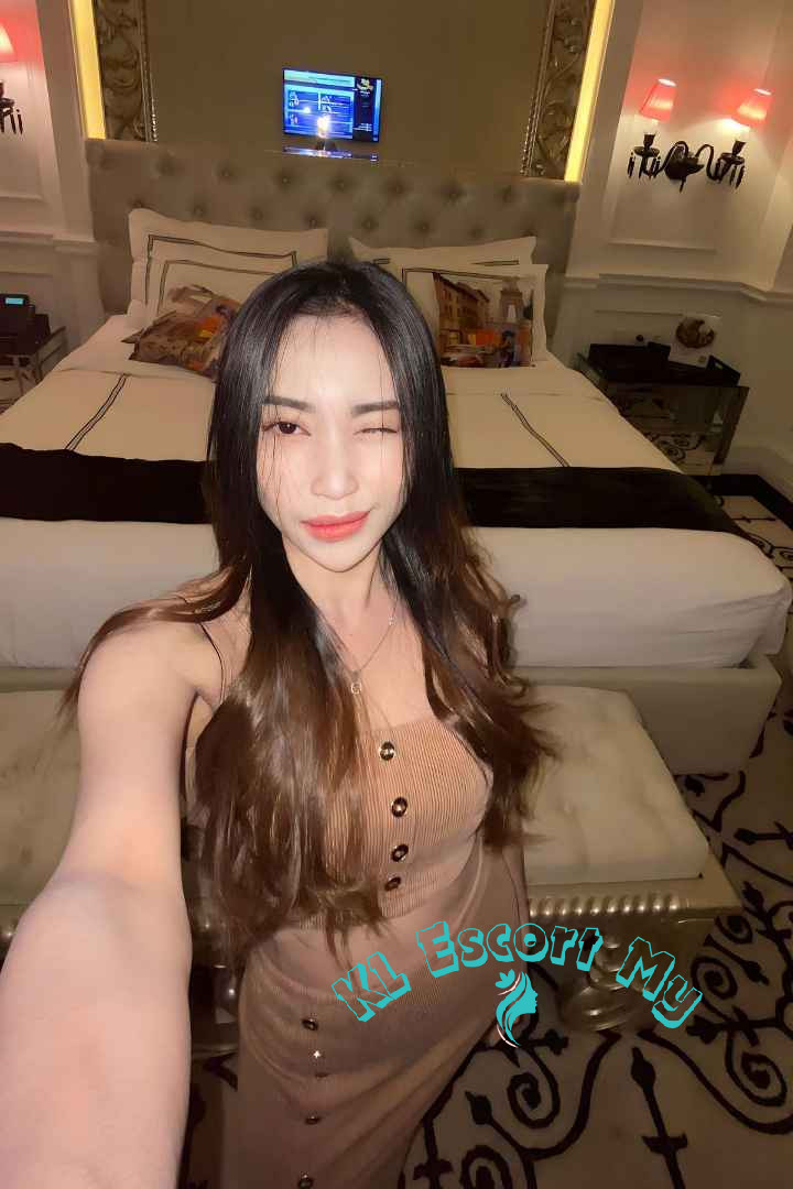 Attractive young woman winking, wearing a beige dress. KL Escort My.