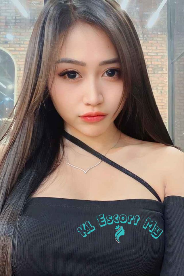 Attractive young woman with long dark hair, wearing a black off-the-shoulder top. KL Escort My