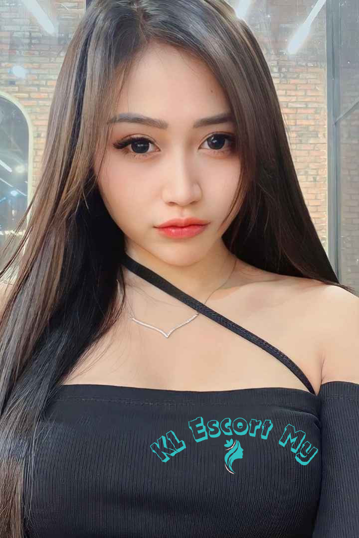 Attractive young woman with long dark hair, wearing a black off-the-shoulder top. KL Escort My